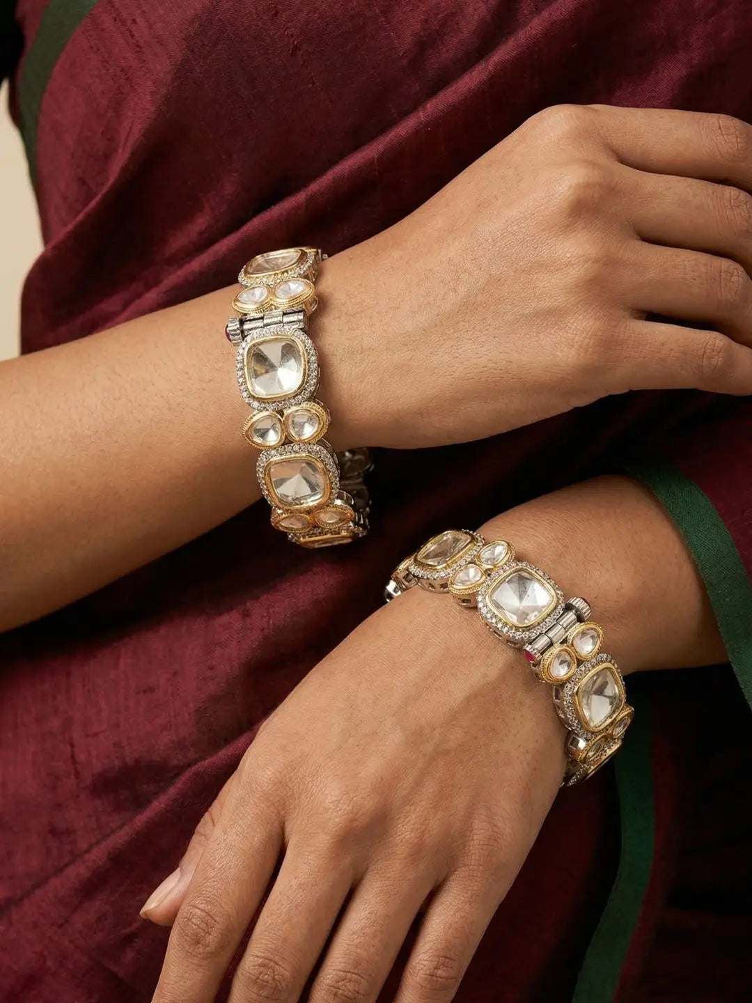 Close-up of hands of a women wearing dual-tone Victorian uncut polki kundan kada bangles on a maroon fabric background