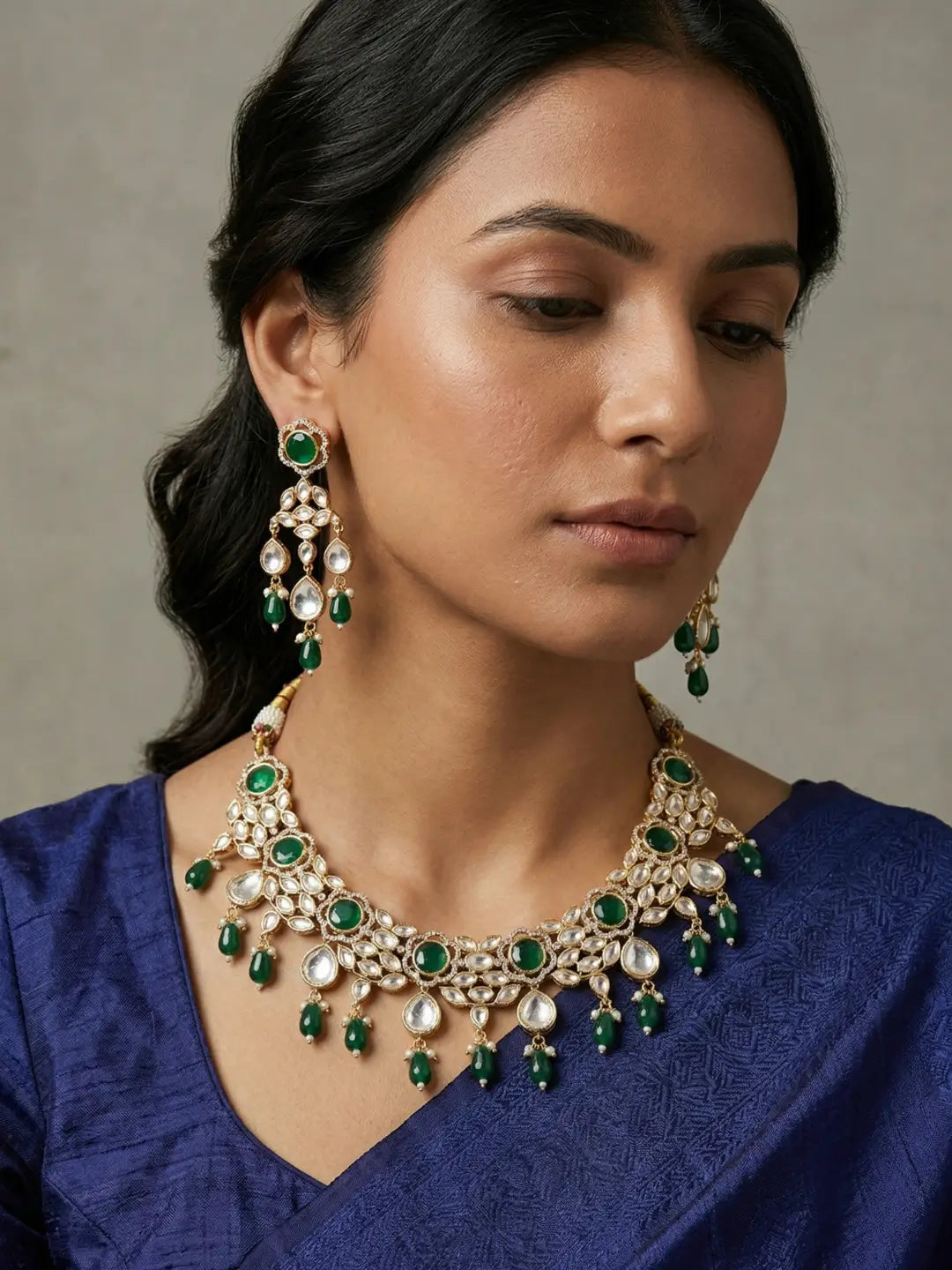 a women wearing an Elegant emerald green Kundan necklace set with matching chandelier earrings featuring premium Kundan stones, green bead drops, and gold-tone finish, perfect for bridal wear, weddings, festive occasions, and traditional Indian jewellery.