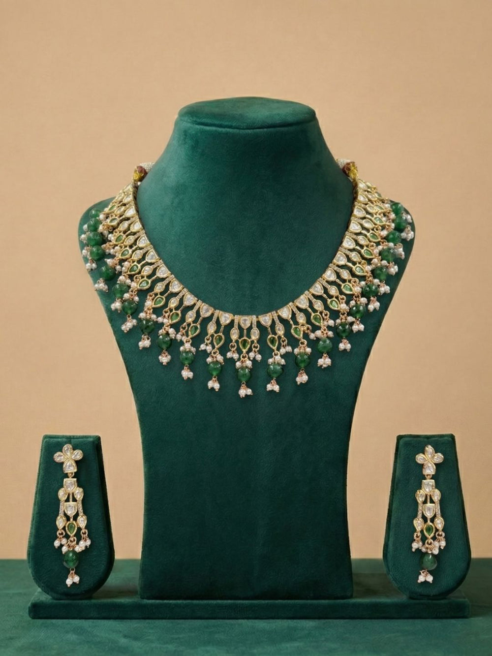 Ornate emerald gren polki kundan necklace set on a green velvet stand with a beige background