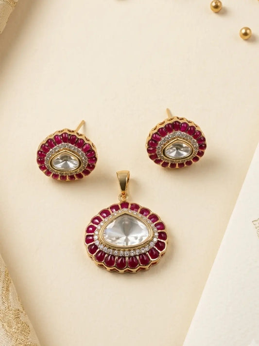 Gold-plated jewelry set featuring a pendant and matching stud earrings decorated with deep red stones and clear central polki  tones, arranged on a light beige textured background.
