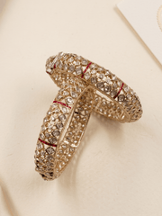 Two ornate gold-toned polki style bangles decorated with clear stones and thin red inlay lines, arranged on a light cream background, handcrafted for women, weddings and festive wear