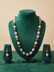 A beaded jewelry set displayed on a dark green velvet mannequin bust and matching stands, featuring a long necklace with pale pink oval beads, white pearl-like beads, and bronze-toned spacer details, plus matching drop earrings.