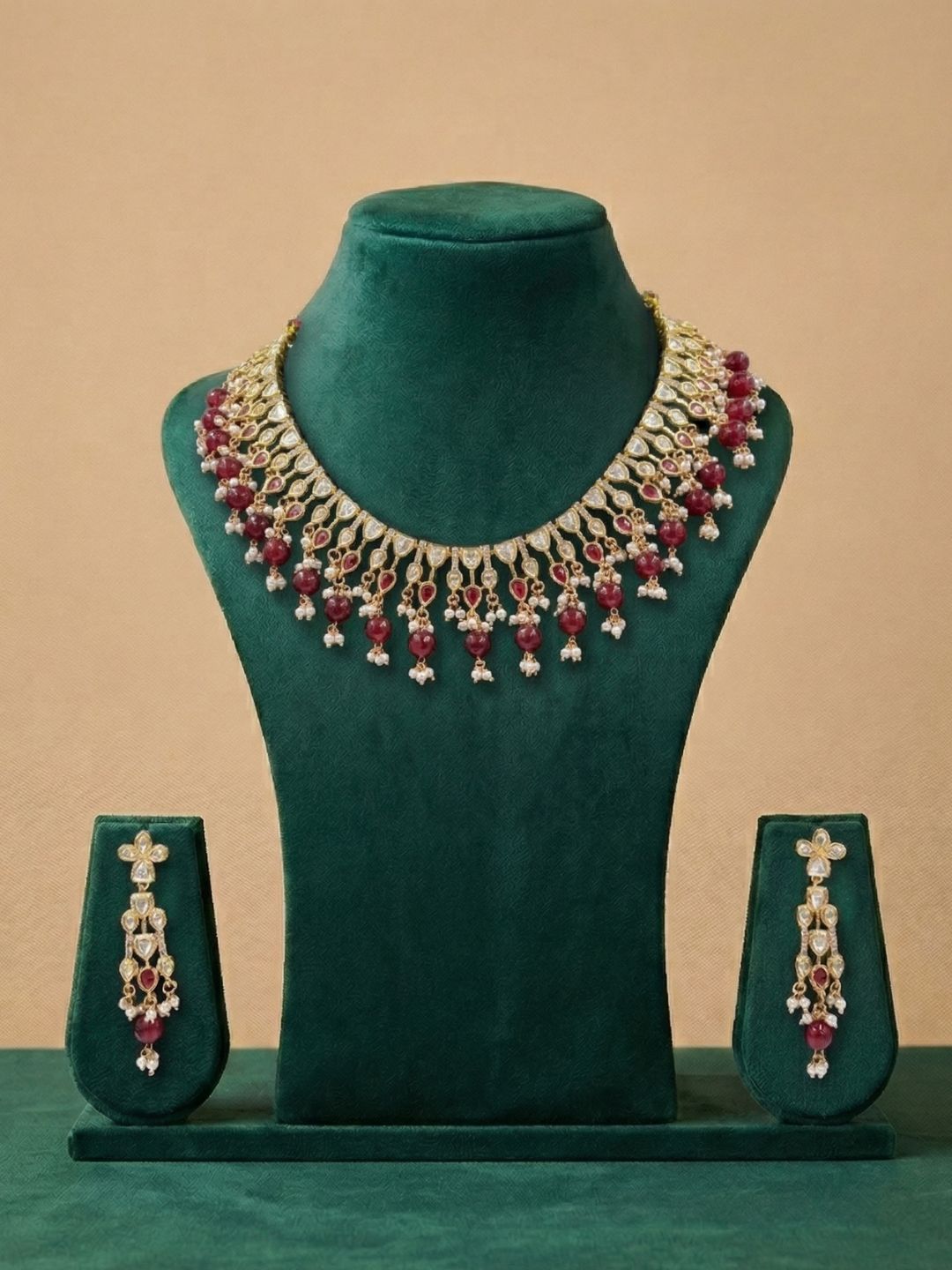 ruby red polki kundan Jewelry set with necklace and earrings on a green mannequin against a beige background