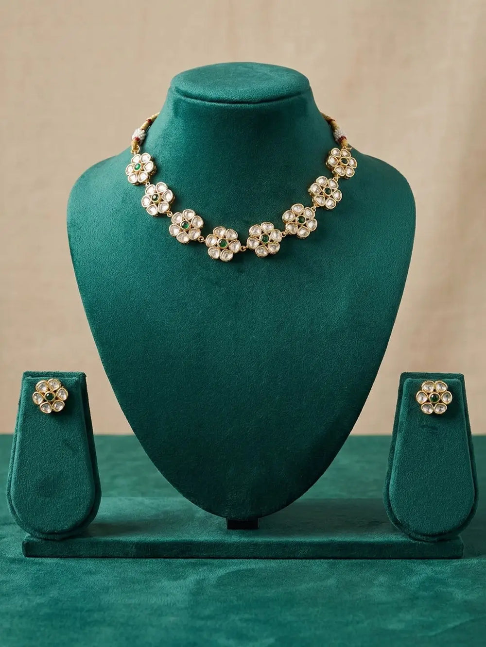 A gold-tone floral design polki necklace and matching stud earrings displayed on a dark teal velvet jewelry bust set against a neutral beige background.