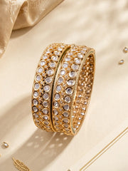 A pair of gold-plated polki-style bangles adorned with clear stones, displayed on a beige textured surface with soft shadows. Wedding, party and festive wear 