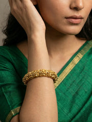 A close-up of a woman wearing an antique gold nakshi bangle bracelet on her wrist, dressed in a green saree with a gold border.