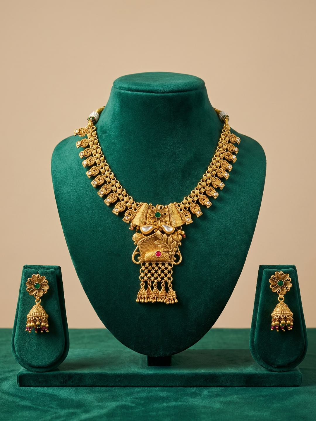 Gold-toned traditional Indian jewelry set displayed on a dark green velvet stand, featuring a heavy necklace with a central peacock pendant and matching drop earrings.