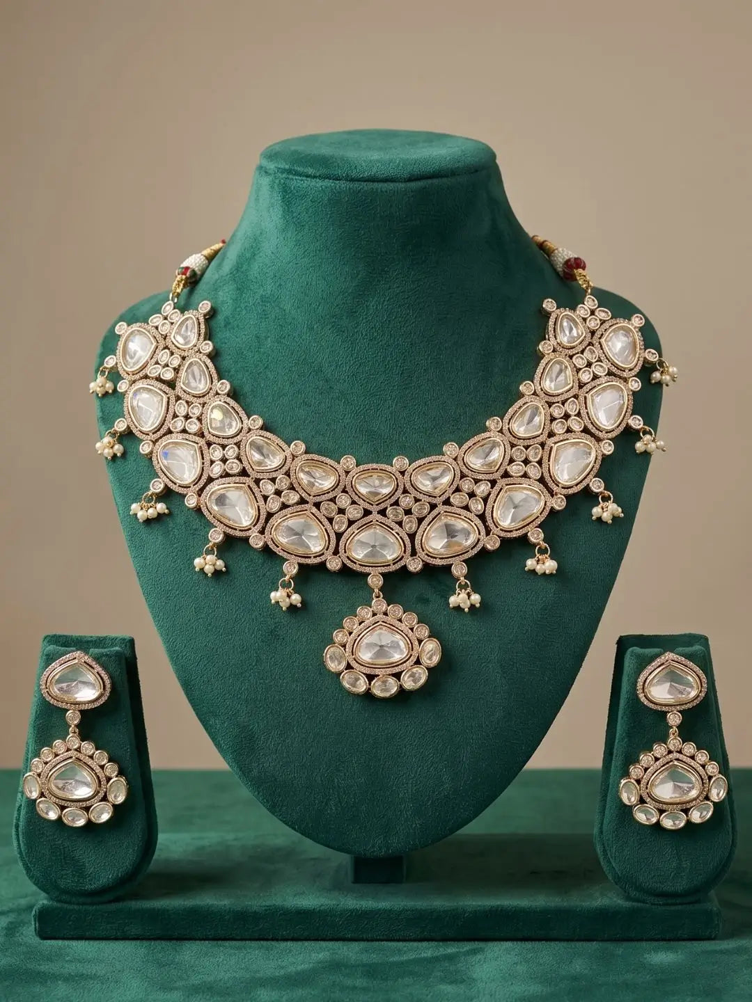 Ornate wedding wear kundan necklace and earrings set on a green mannequin against a beige background