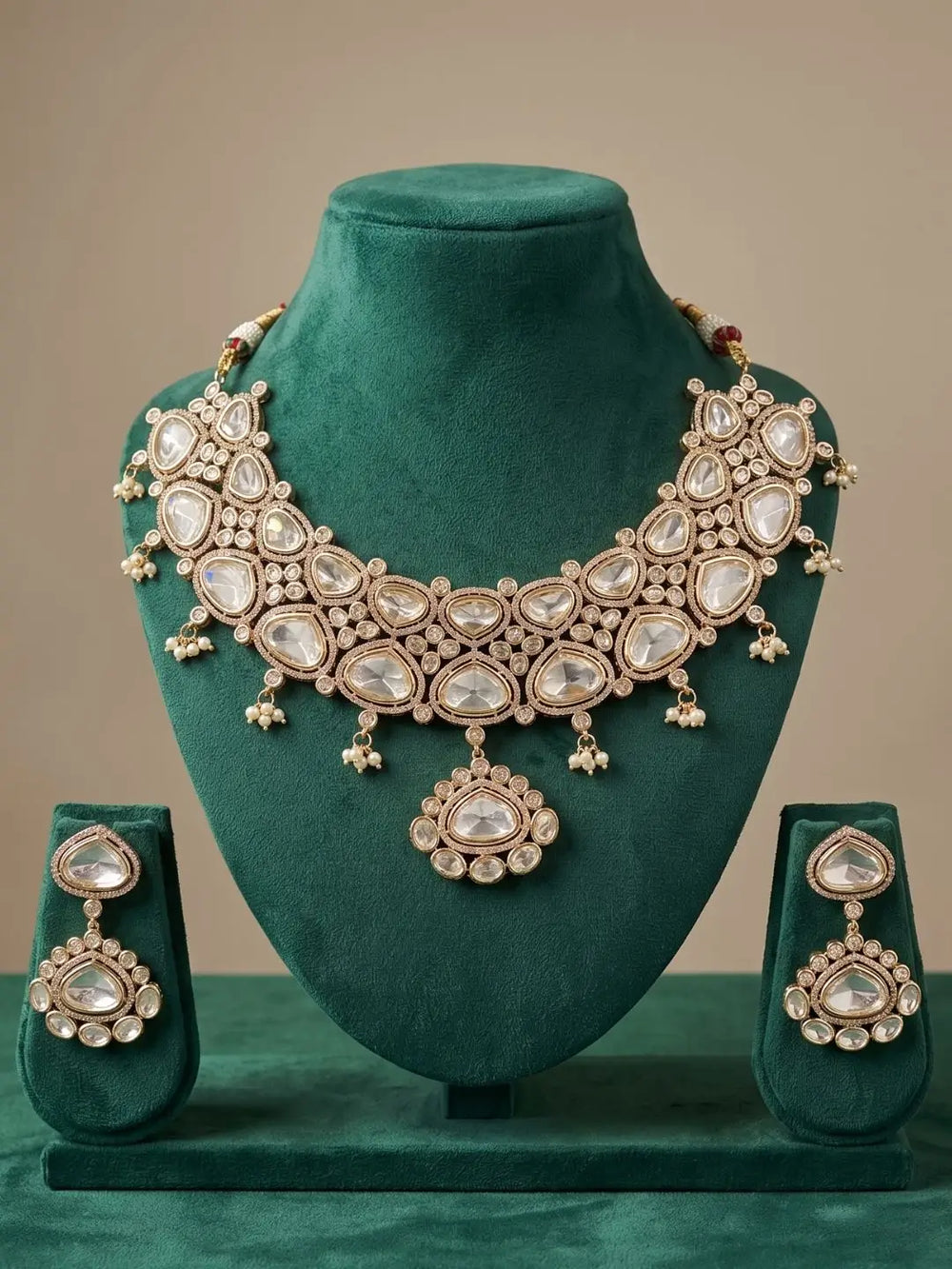 Ornate wedding wear kundan necklace and earrings set on a green mannequin against a beige background