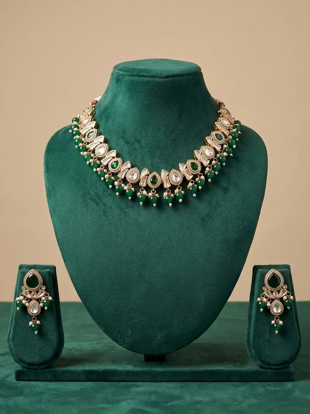 A traditional Indian kundan jewelry set featuring a statement necklace and matching earrings, displayed on a dark green velvet jewelry bust and stand against a solid beige background.