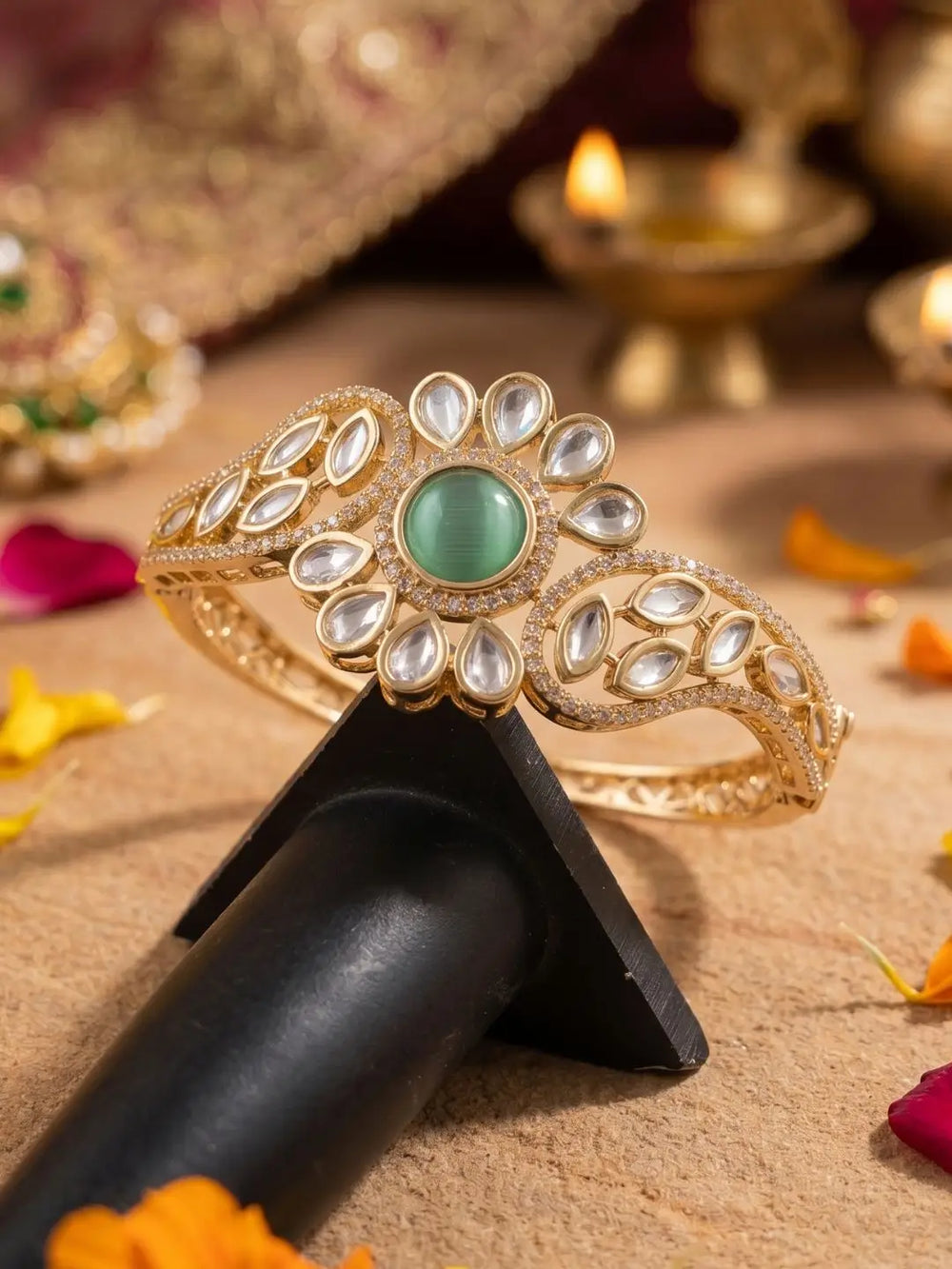 Gold-plated kundan bracelet with green gemstone on a black stand, with Diwali decorations in the background.