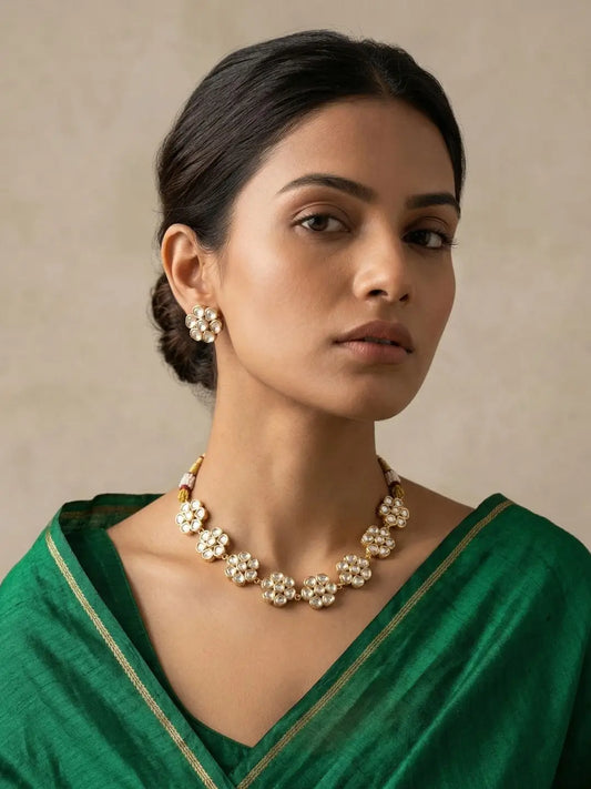Woman wearing a green saree with gold-plated flower-design polki necklacs set  inst a neutral background