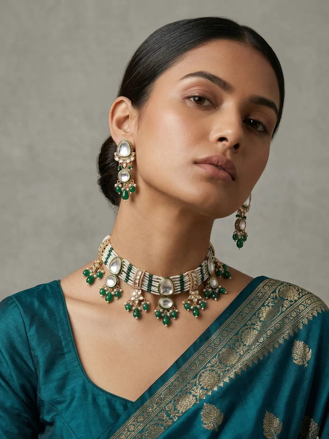 a women is wearing handcrafted multi-strand Kundan Pearl choker necklace set with matching earrings featuring emerald green bead accents, perfect for bridal wear, weddings, festive occasions, and traditional Indian jewellery.