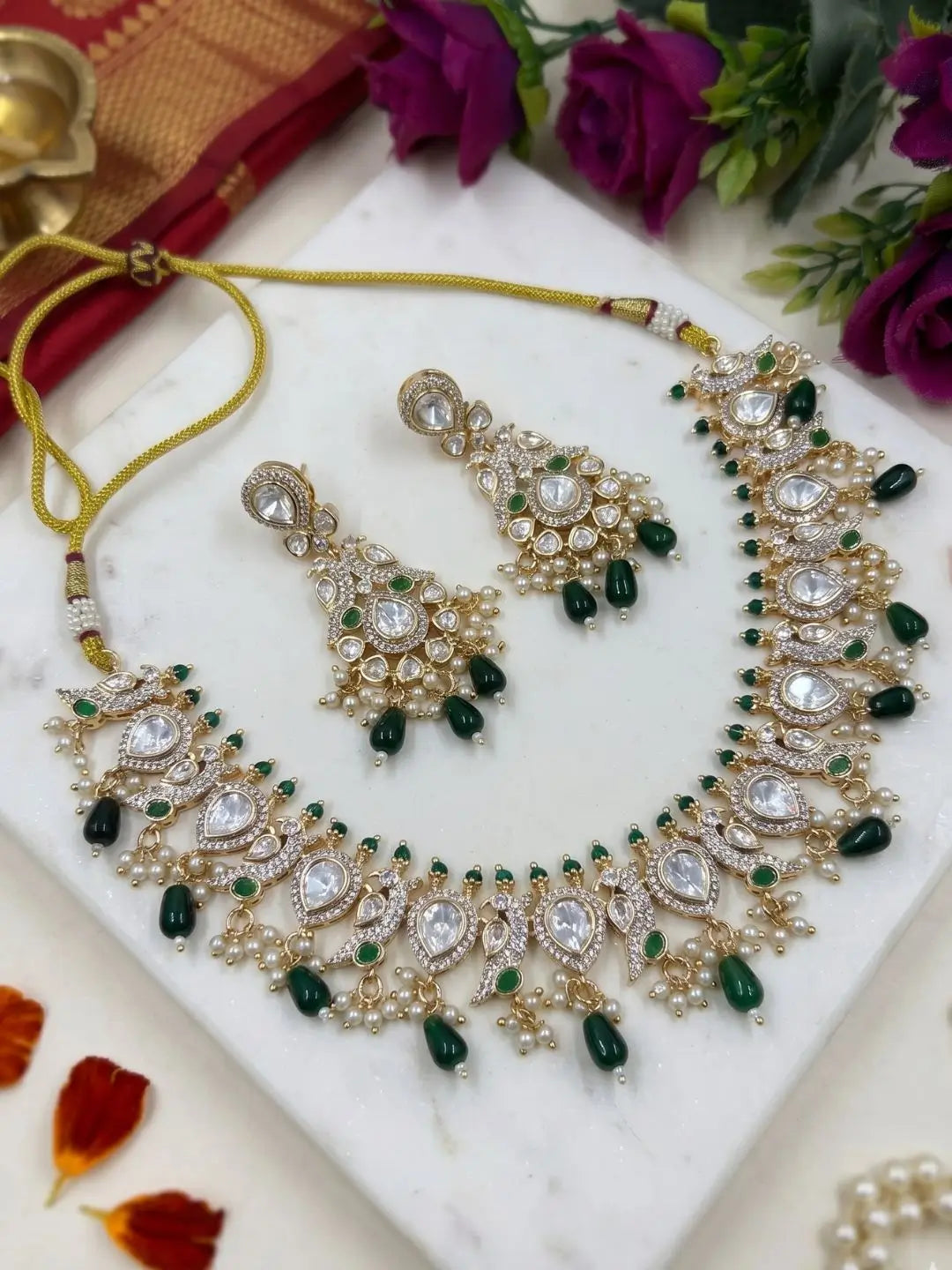 Ornate green peacock design polki necklace and earrings set with green stones on a white marble surface.