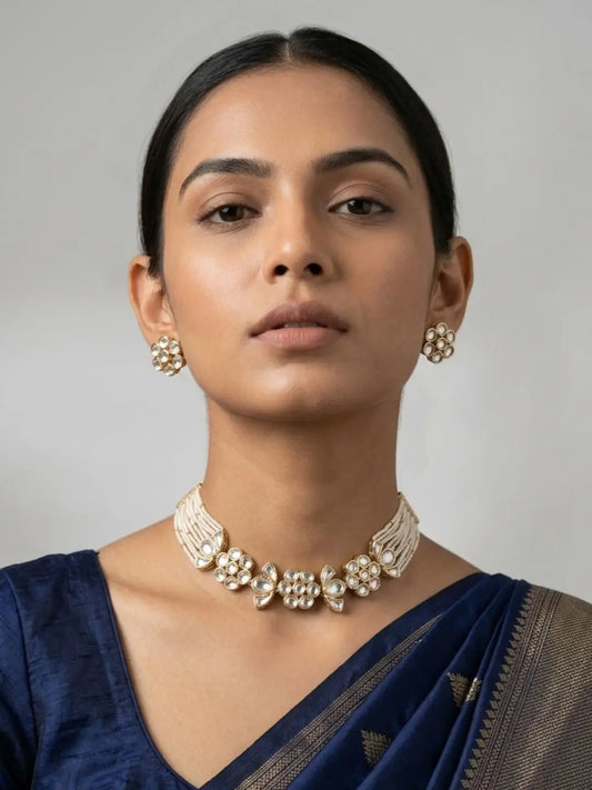 Woman wearing a blue saree with a white kundan pearl choker necklace and earrings against a gray background