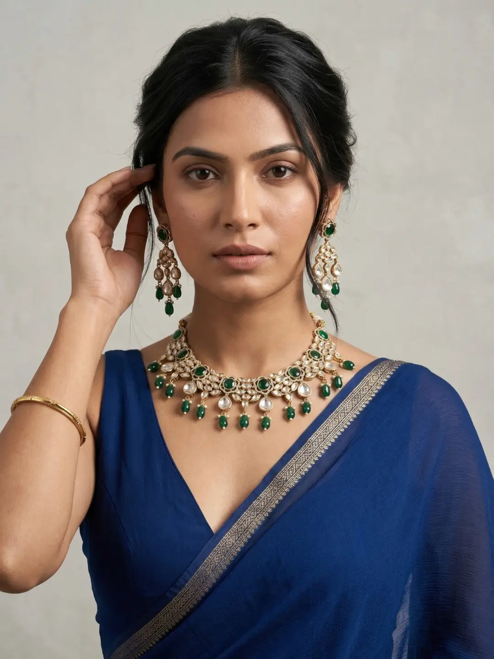 a women in a blue saree wearing an Elegant emerald green Kundan necklace set with matching chandelier earrings featuring premium Kundan stones, green bead drops, and gold-tone finish, perfect for bridal wear, weddings, festive occasions, and traditional Indian jewellery.