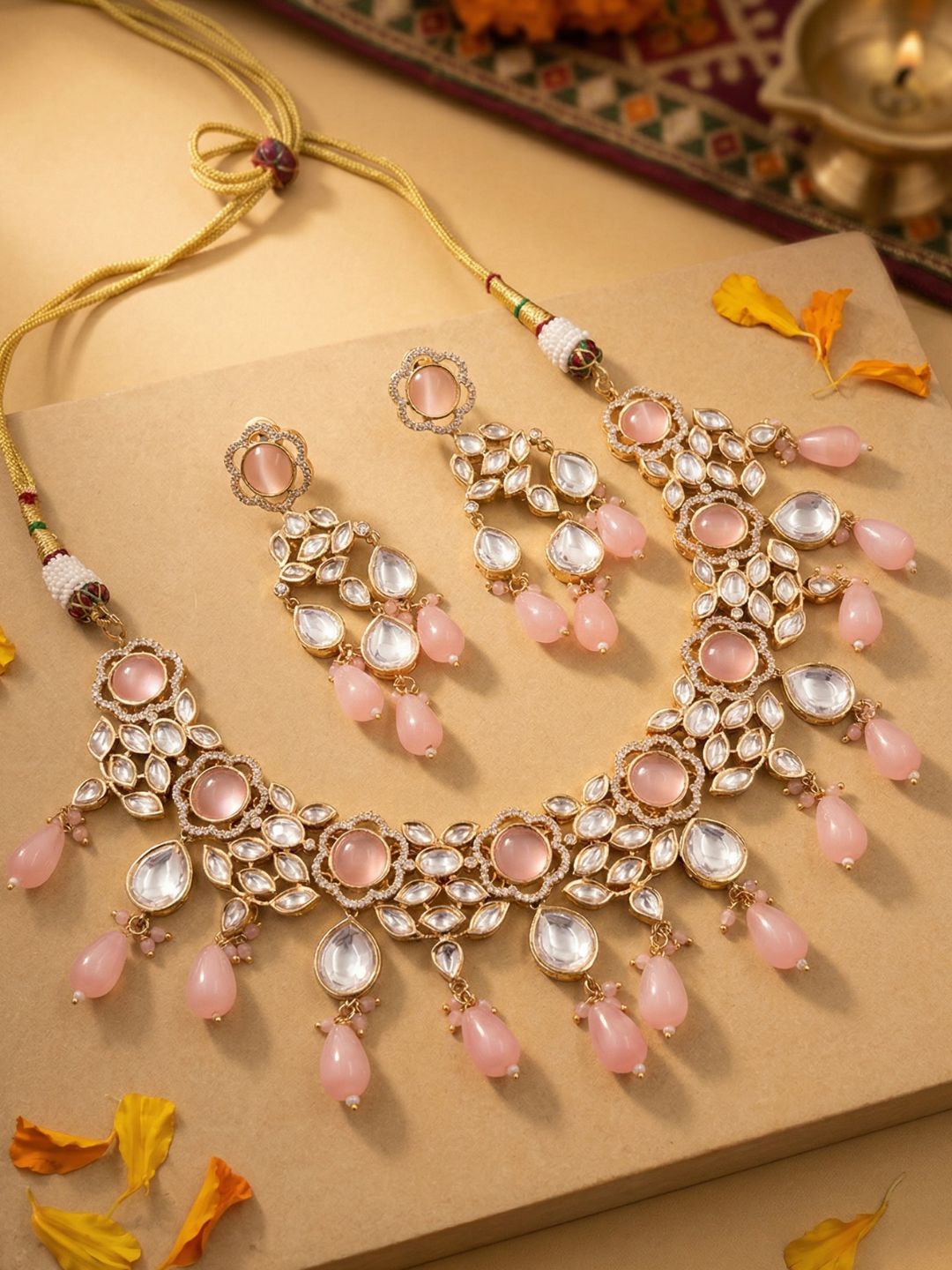 Ornate gold plated kundan necklace and earring set with pink stones and pink beaded drops on a textured surface