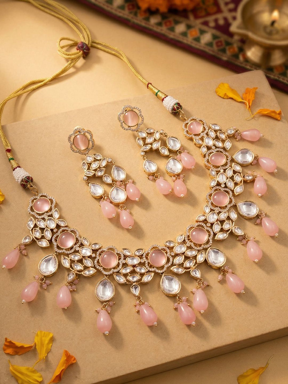 Ornate gold plated kundan necklace and earring set with pink stones and pink beaded drops on a textured surface