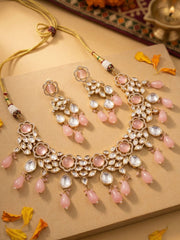 Ornate gold plated kundan necklace and earring set with pink stones and pink beaded drops on a textured surface