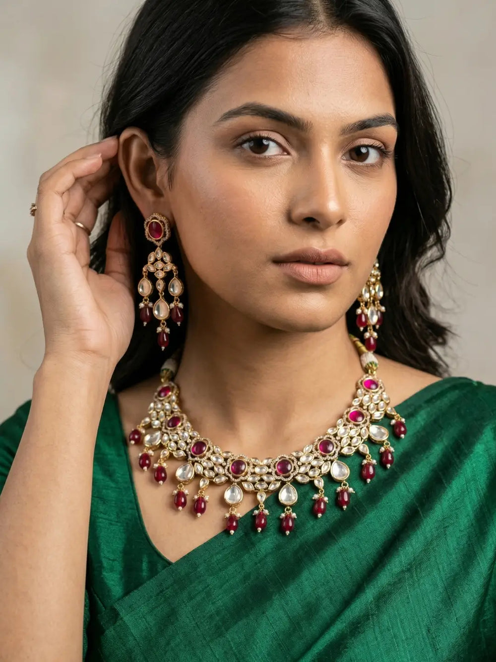 a women in a green saree wearing an Elegant Ruby pink Kundan necklace set with matching chandelier earrings featuring premium Kundan stones, red bead drops, and gold-tone finish, perfect for bridal wear, weddings, festive occasions, and traditional Indian jewellery.