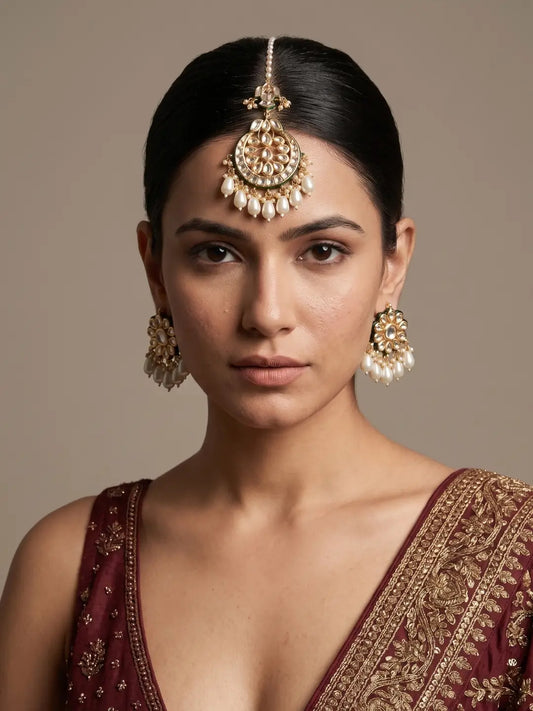 A women in a red bridal saree is wearing a gold plated kundan maang tikka and earring set 
