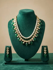 A green and gold traditional Indian jewelry set displayed on a dark green velvet mannequin bust, featuring a multi-strand pearl and green stone necklace with matching drop earrings.