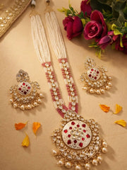 An ornate Indian long bridal jewelry set displayed on a beige surface, featuring a long necklace with a large circular pendant, matching earrings, and pearl strands, decorated with gold, white stones, and red accents, styled with flowers and orange petals.