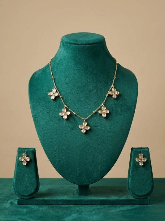 A gold-tone floral statement chain necklace and matching stud earrings displayed on a dark teal velvet jewelry stand set against a solid beige background.