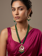 A woman wearing a green beaded necklace with a large gold plated mop pendant, matching drop earrings, and a magenta satin blouse against a neutral background.