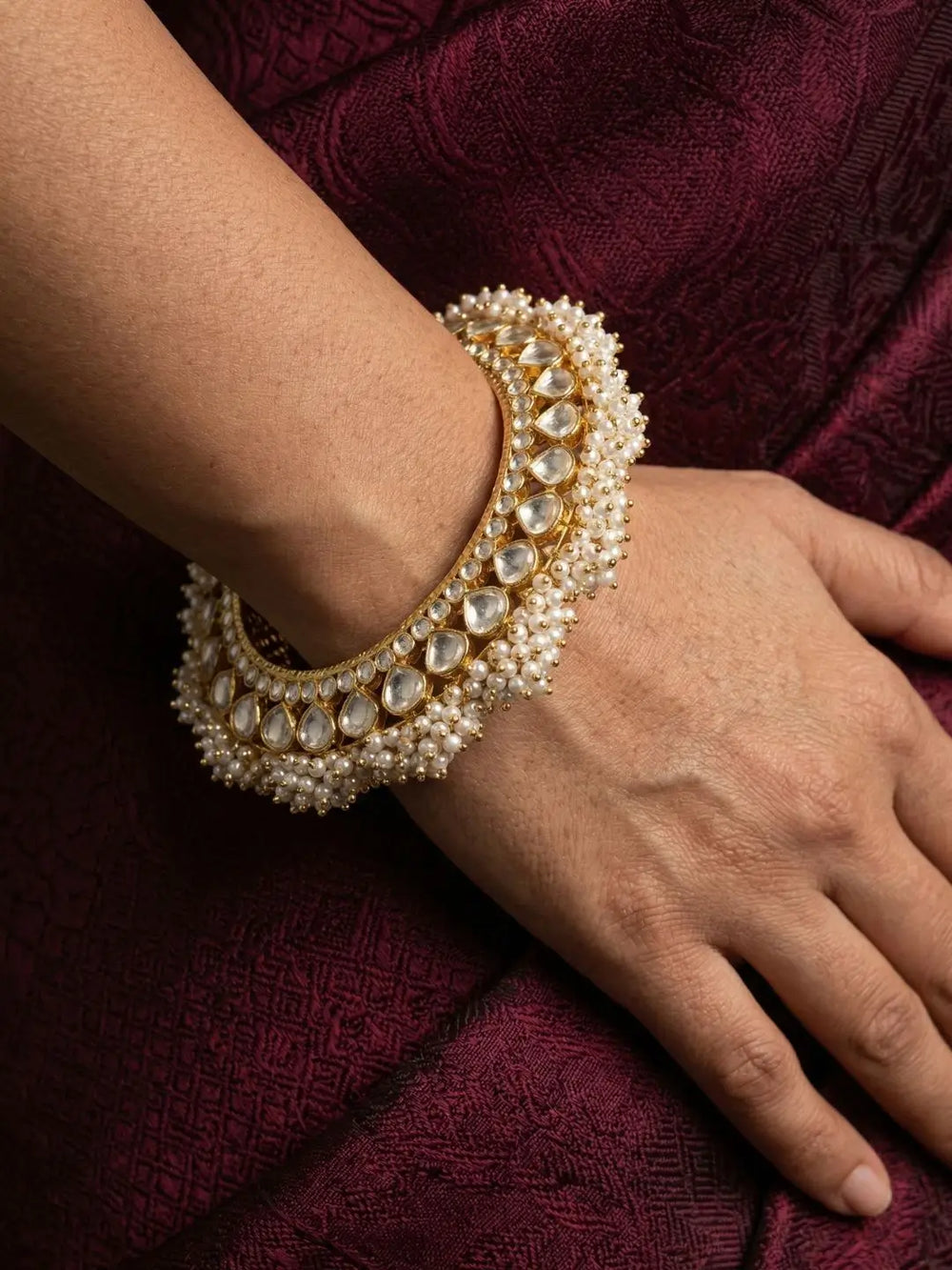 gold-plated paachi kundan jadau gokhru bracelet on a wrist against a dark fabric background