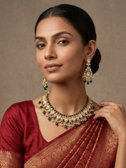 Woman wearing traditional green peacock design polki jewelry set and a saree against a neutral background