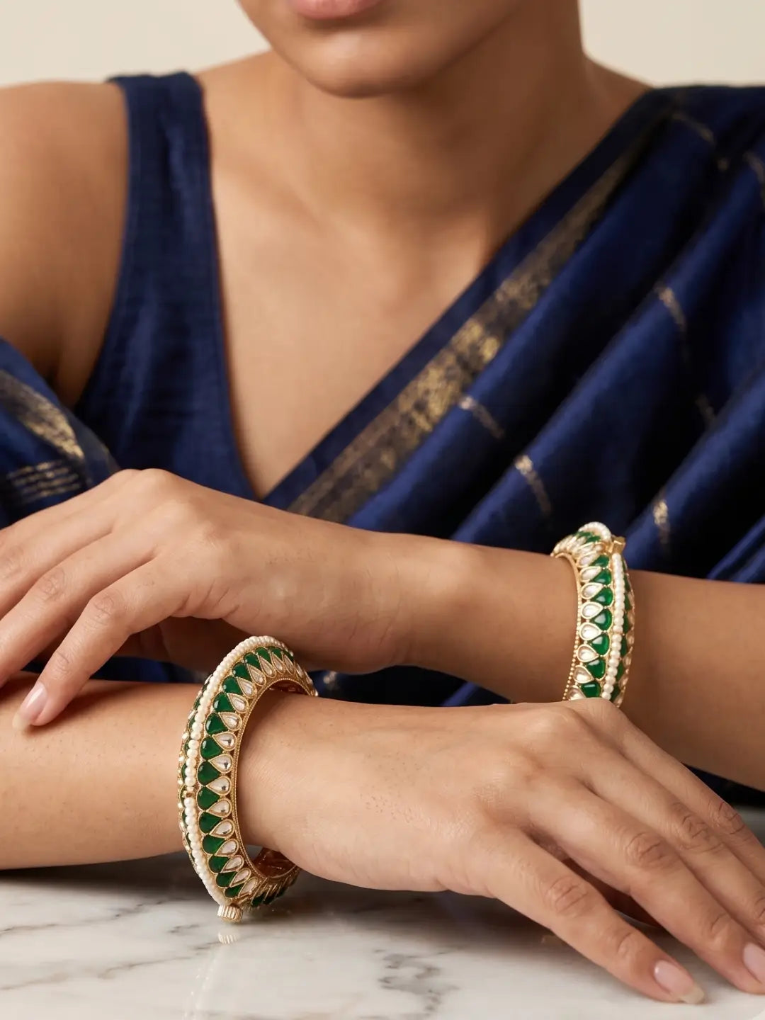 a close up portrait of a women wearing Handcrafted gold-plated Kundan bangles featuring sparkling Kundan stones, elegant pearl borders, and emerald green enamel detailing, perfect for bridal wear, weddings, festive occasions, and traditional Indian jewellery.