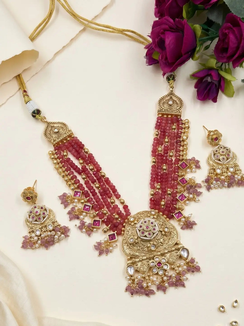 Ornate red and gold necklace with matching earrings on a white surface with purple flowers.