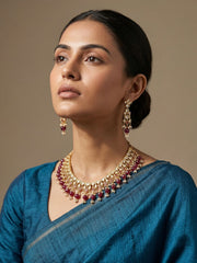 A women wearing a gold plated ruby pink kundan polki necklace and earring set on a blue saree