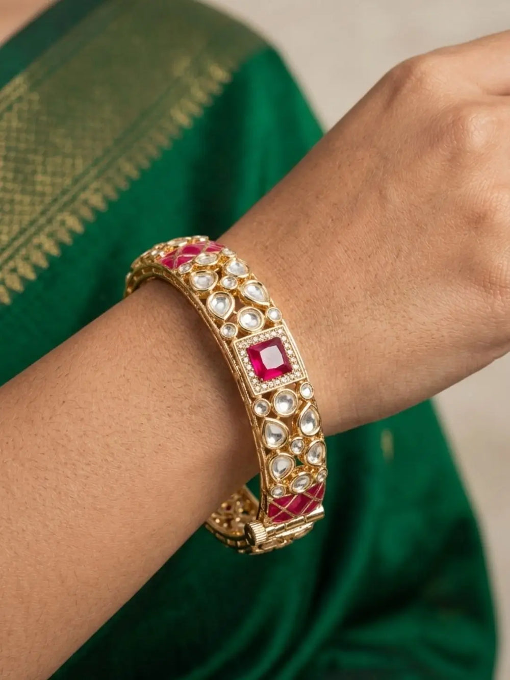 Gold-plated bangles with red and white polki stones worn on a wrist against a green saree background