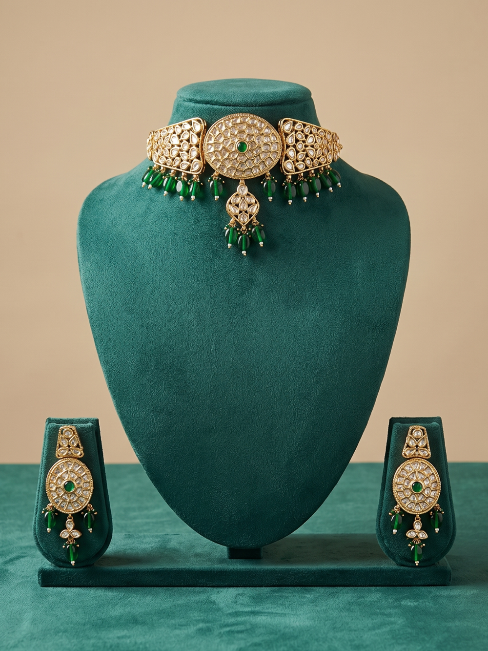 A traditional Indian choker jewelry set displayed on a dark teal velvet mannequin bust. The set includes a choker necklace with a large central oval motif, three side oval motifs, and dangling green bead fringes, along with matching earrings, all embellished with gold and clear stones.