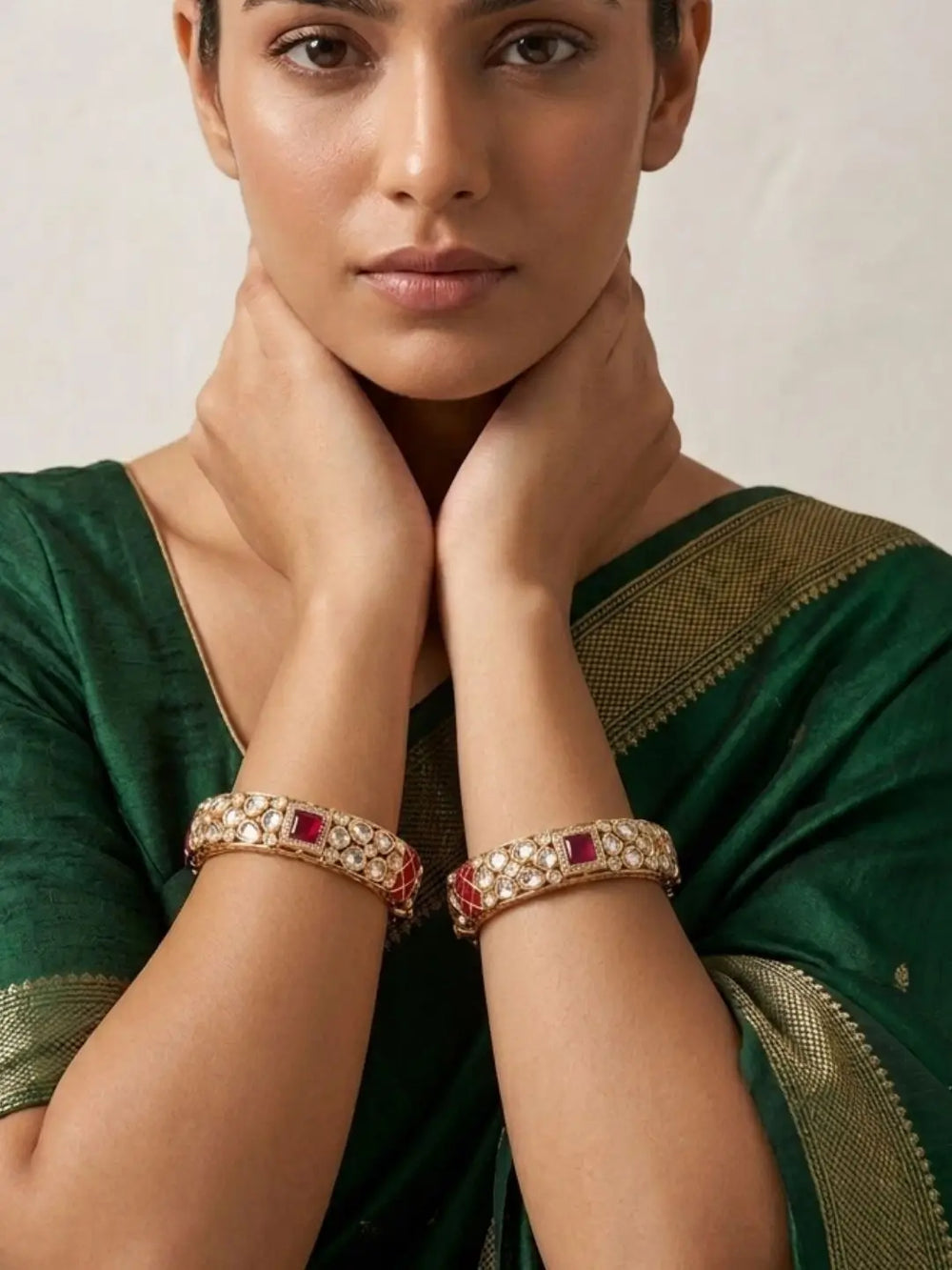 Woman wearing a green saree with gold border and gold-plated ruby kundan studded bangles on a neutral background
