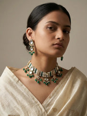 A woman wearing a traditional Indian outfit with a cream-colored saree, showcasing a gold and green beaded choker necklace and matching drop earrings.