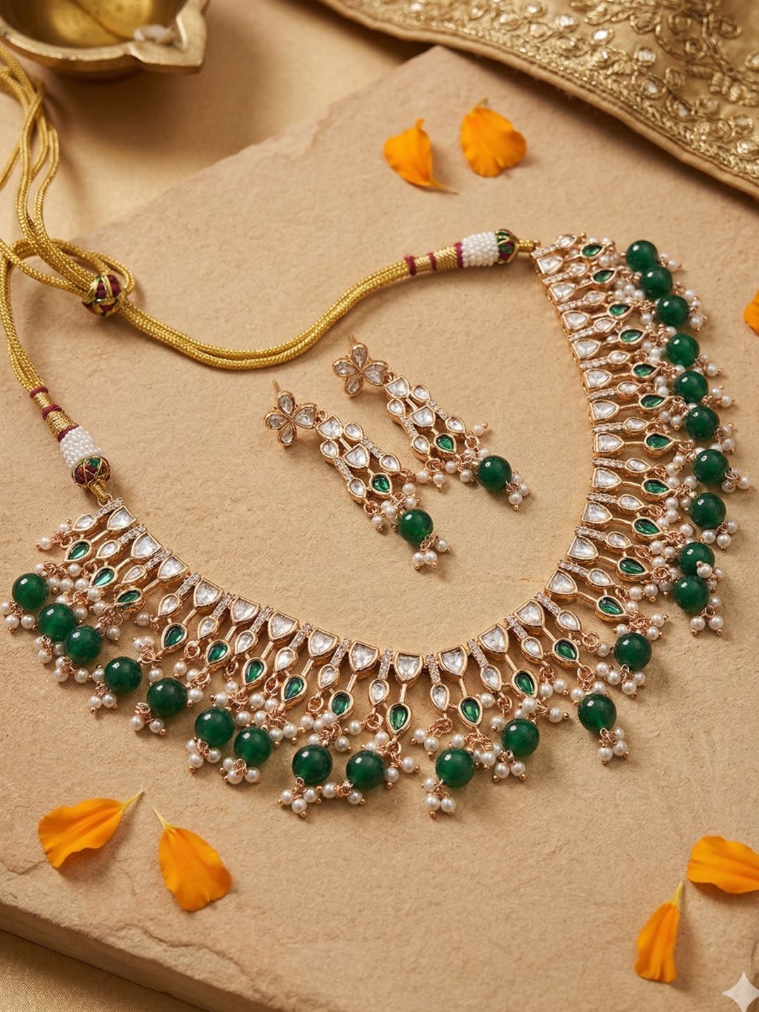 Ornate polki kundan necklace and earrings with green beaded stones on a beige surface with orange petals.