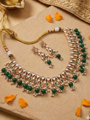 Ornate polki kundan necklace and earrings with green beaded stones on a beige surface with orange petals.