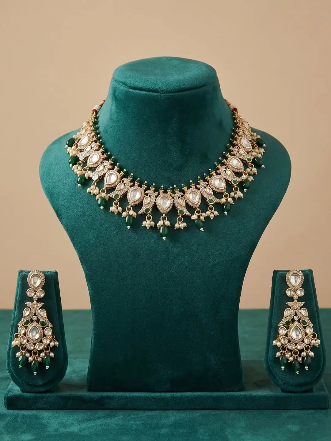Ornate necklace and earrings set on a green velvet stand against a beige background