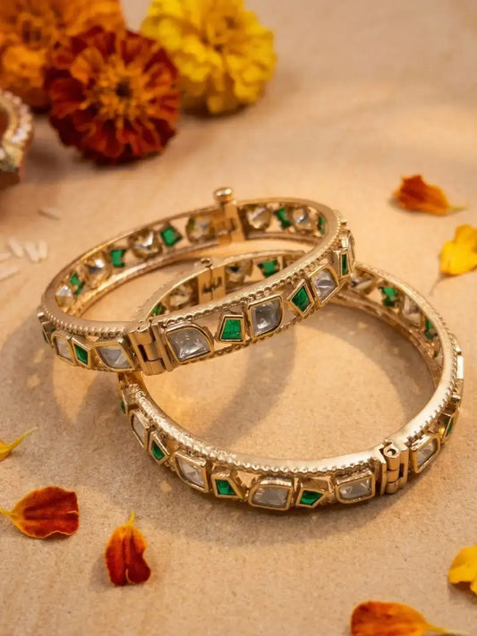 Gold plated uncut polki and green stones studded bangles  on a textured surface with dried flowers.