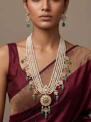 A woman in  red saree is wearing an Elegant multi-layer pearl long necklace set featuring a handcrafted Kundan pendant with emerald green bead drops, ruby-inspired centre stone, and matching earrings, perfect for bridal wear, weddings, festive occasions, and traditional Indian jewellery.