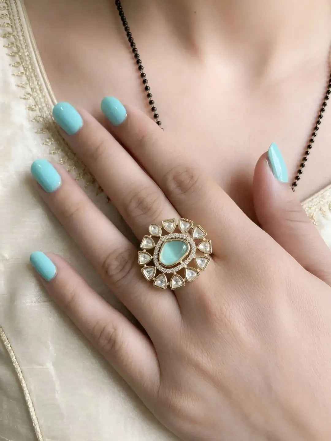Hand wearing a polki ring with a mint green stone on a neutral background