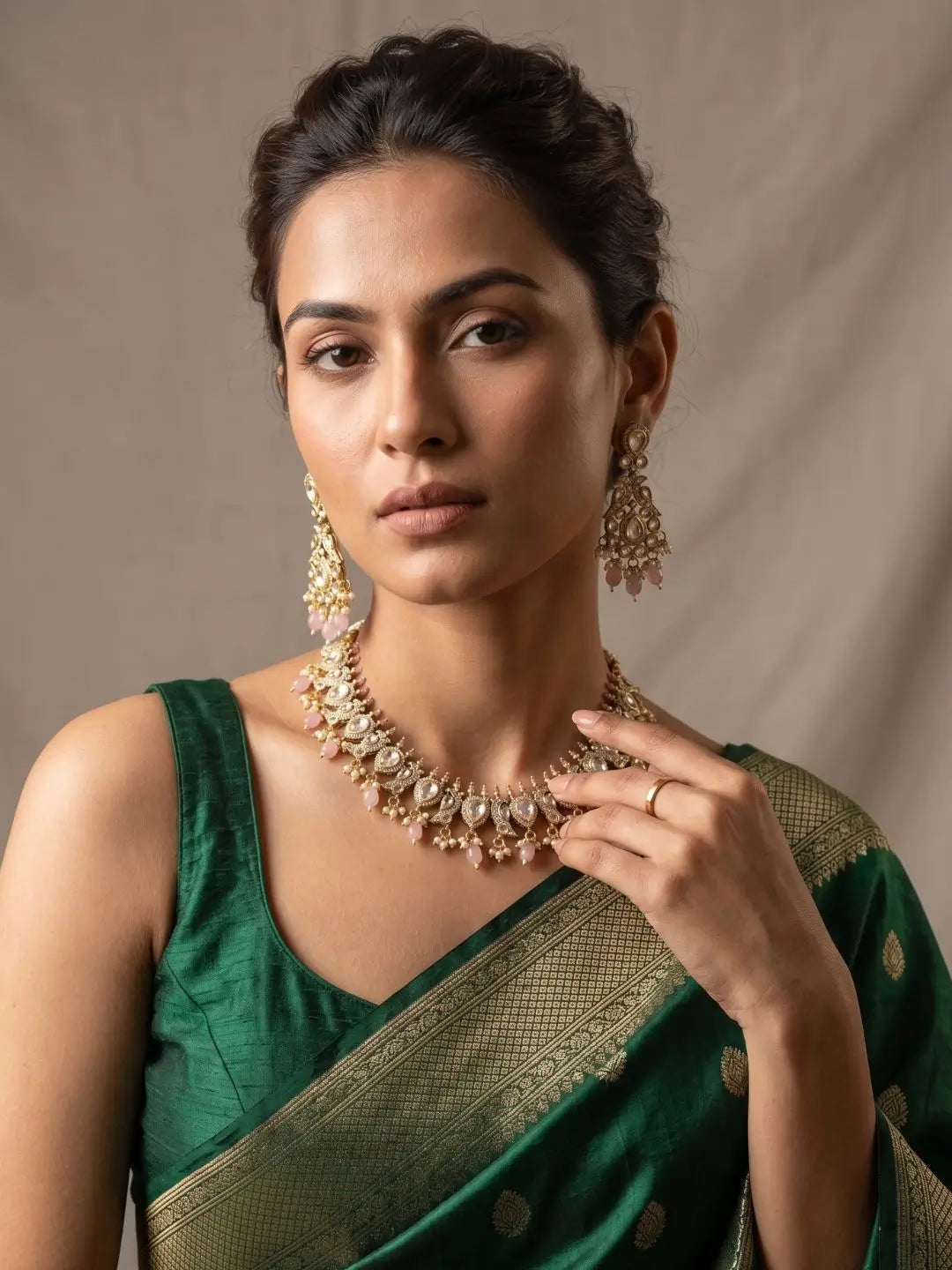 Woman wearing a green saree with gold-plated polki jewelry against a neutral background