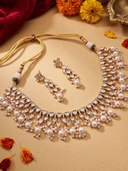 gold plated white kundan and Pearl necklace and earrings set on a beige surface with flowers in the background