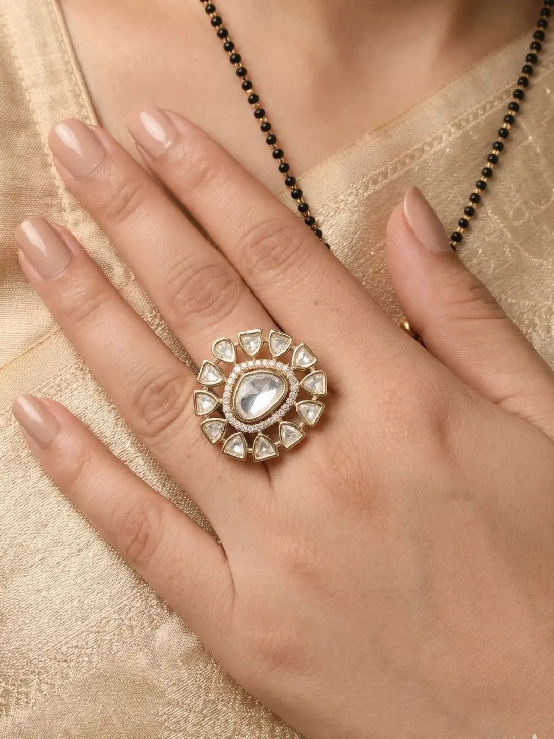 Close-up of a hand wearing a polki ring with a heart-shaped center on a beige fabric background.
