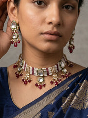 A close-up of a woman wearing a traditional Indian gold-plated red choker necklace and matching drop earrings with white stones and red beads, paired with a navy blue saree.