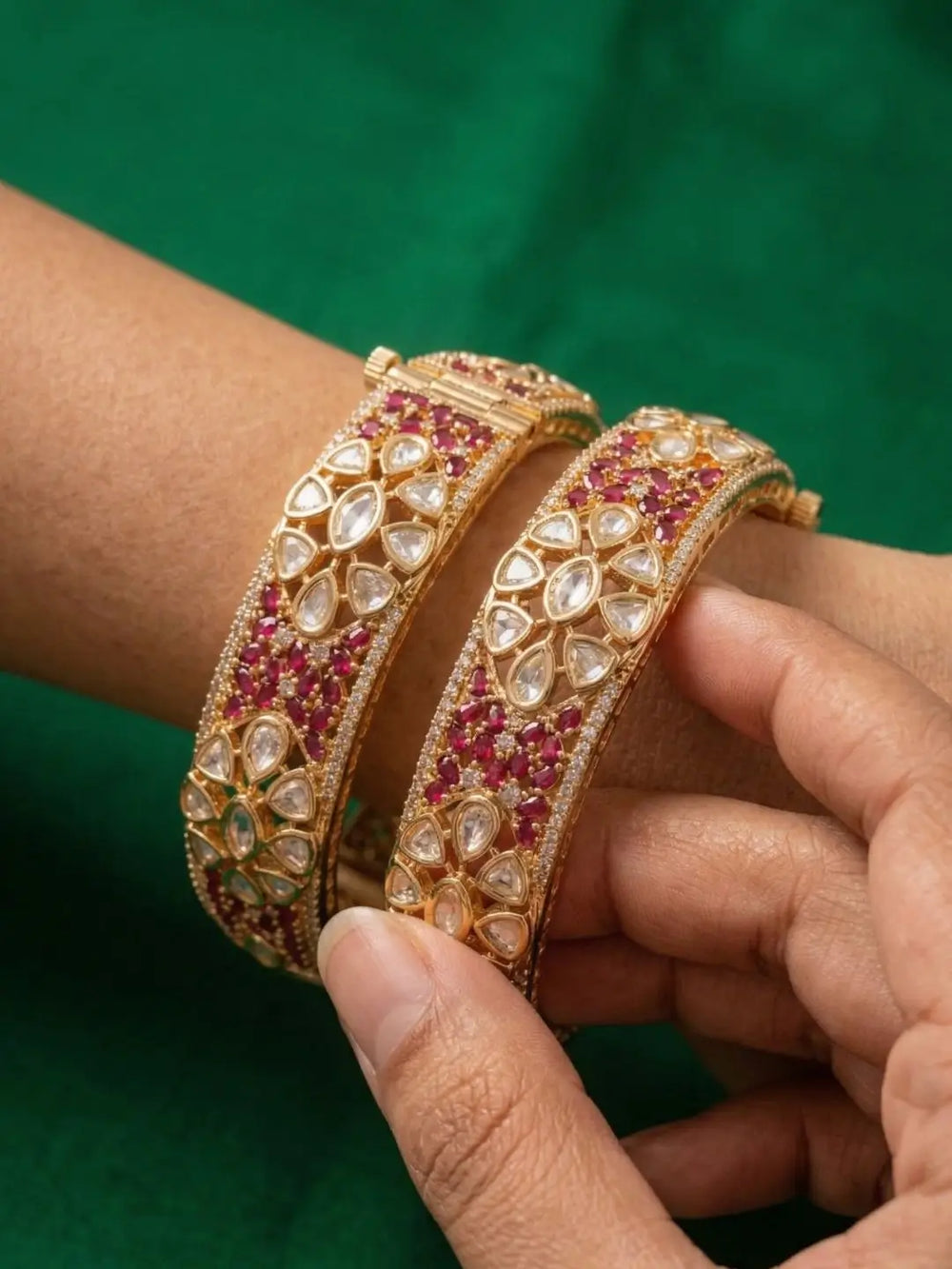 Gold bangles with red and white stones on a green background