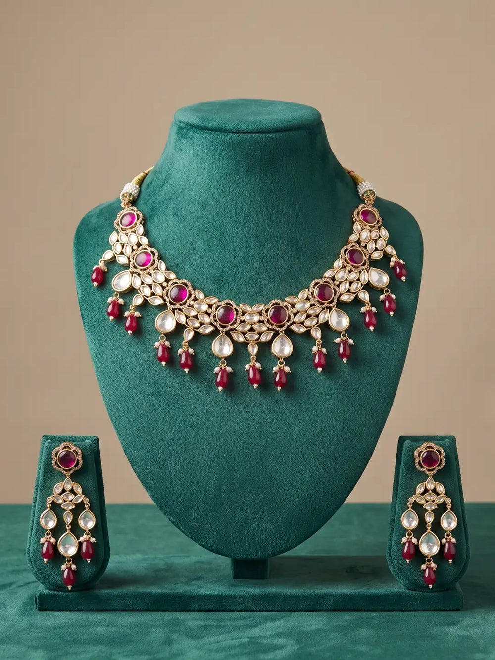 Gold-toned Indian Kundan jewelry set featuring a statement necklace and matching drop earrings displayed on a teal velvet jewelry bust. 